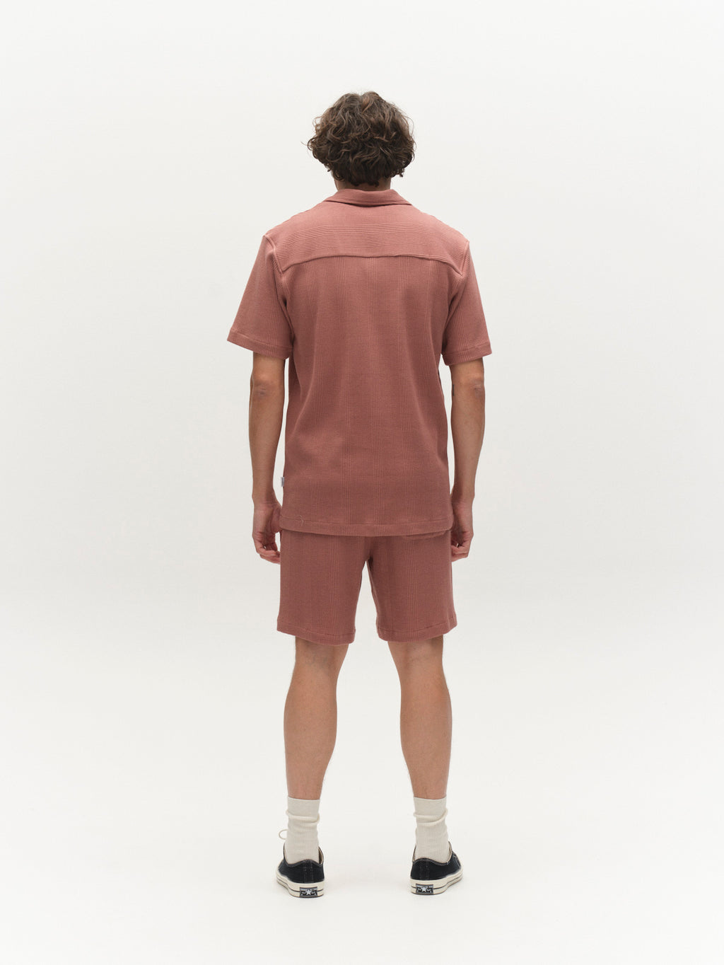 A person stands facing away, wearing the Gabba GABvalente Wup SS T-Shirt in Wood Pink with a relaxed fit, white socks, and black sneakers, set against a plain white background.