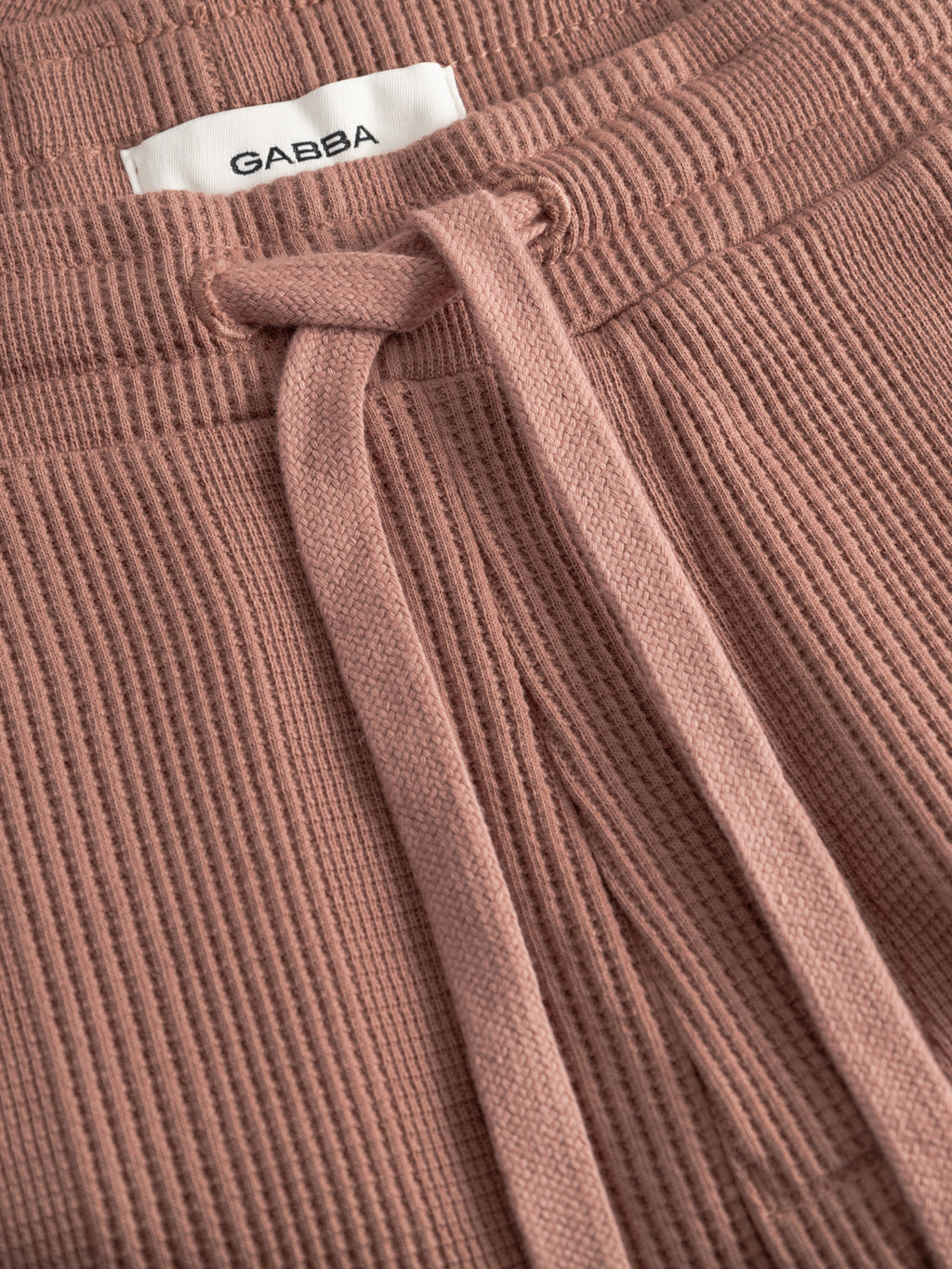Close-up of ribbed, wood pink GABtommi Wup Shorts by Gabba, featuring an elastic waistband with drawstring and a white Gabba label sewn inside.