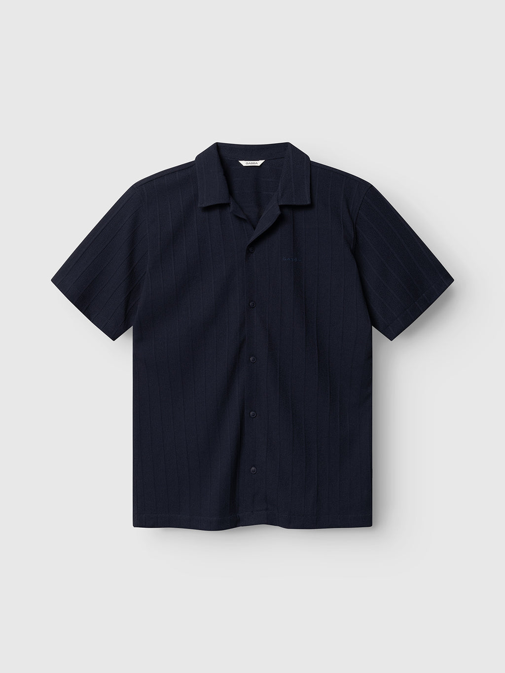 The Gabba GABvalente Armor SS T-Shirt in navy features a relaxed fit, short sleeves, and subtle vertical pinstripes, with a resort collar and cotton-blend fabric, presented on a light gray background.