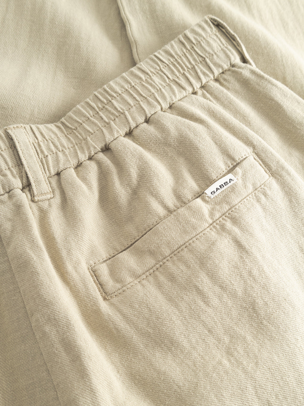 Close-up of GABnapoli 19 Lino Pant - Alfa Green by Gabba, featuring a beige elastic waist, back pocket with a small white SARBA label, soft textured fabric, and visible stitching for a casual look.
