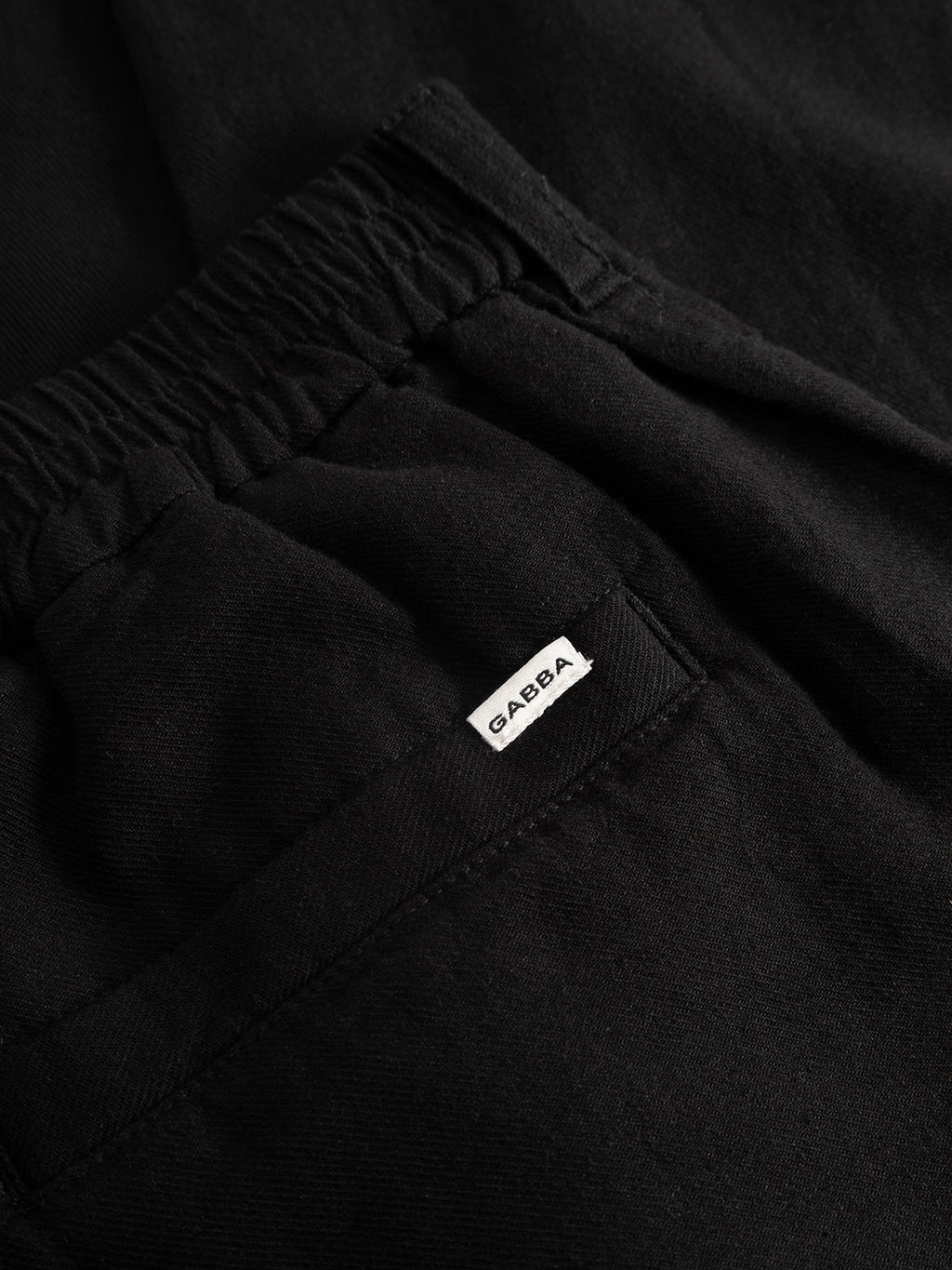 Close-up of Gabba’s GABnapoli 19 Lino Pant in Meteorite—black straight-fit chinos with an elastic waistband, pocket, and visible lightweight texture. A small white label on the pocket reads GAËBA.