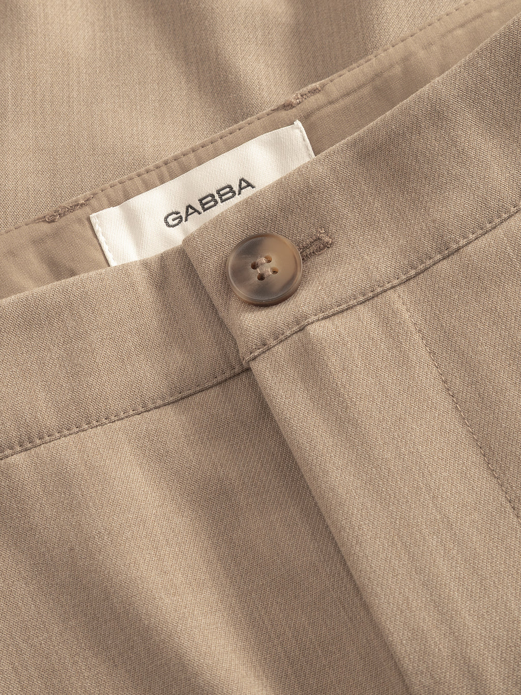Close-up of Gabba GABjoli Pas Phin Shorts GRS in Sand Plaza shows smooth, slightly textured beige fabric, brown button, and a white inner waistband tag labeled Gabba for a tailored finish.