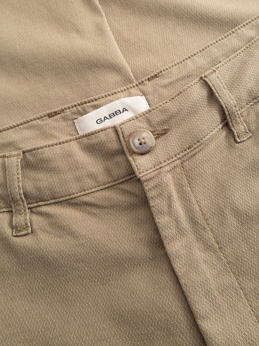 Close-up of Gabba’s GABjoe Nopleats Dale Pant in sand: tapered-fit chinos in high-stretch cotton blend with a visible button, belt loops, waistband, and inner white Gabba label for a modern look.