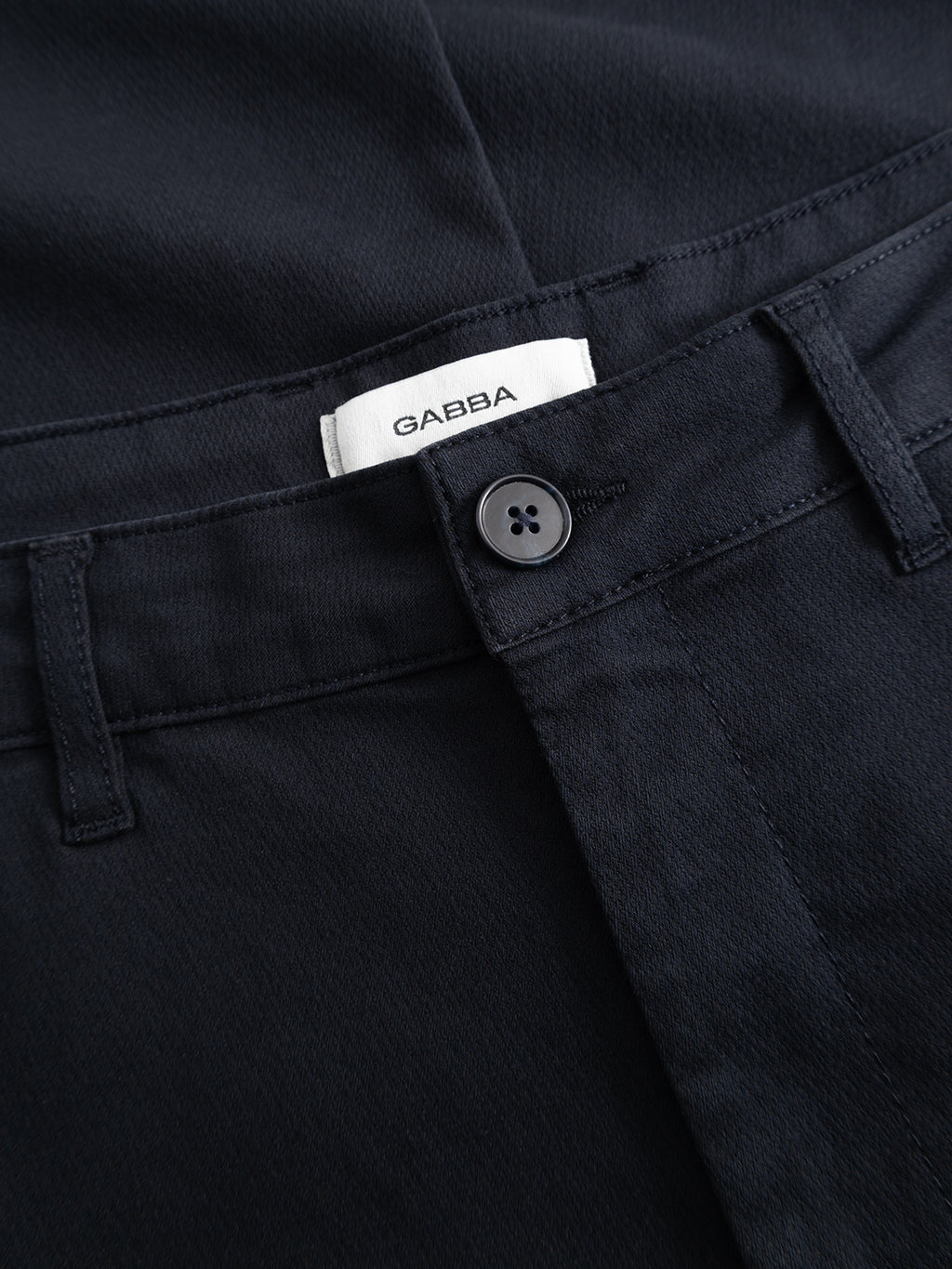 Close-up of Gabba’s GABjoe Nopleats Dale Pant in blue black—a tapered-fit chino crafted from high-stretch cotton-blend with belt loops, black button, and a white GABBA label, perfect for the modern wardrobe.