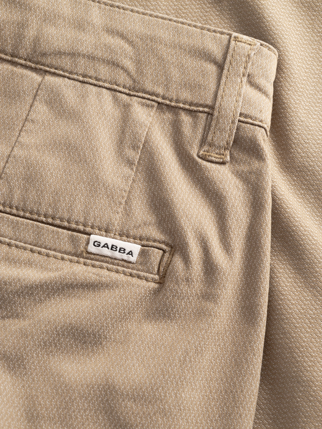 Close-up of GABjoli Nopleats Dale Shorts in sand by Gabba, highlighting the textured fabric, back pocket with a white GABBA label, and visible belt loop at the waist.