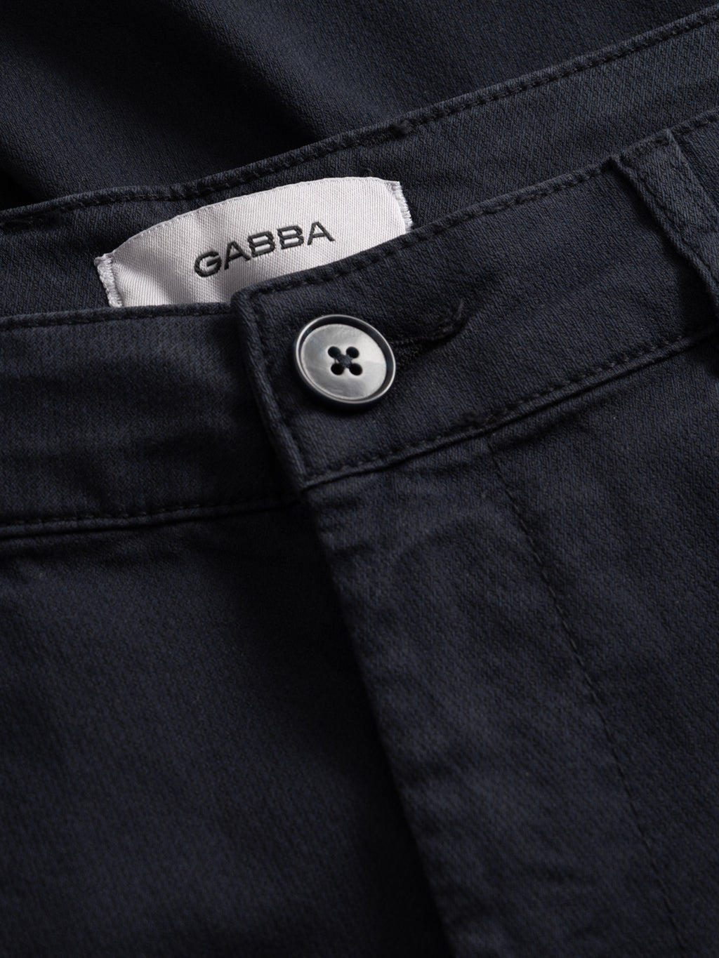 Close-up of blue black GABjoli Nopleats Dale Shorts with a visible button and a white waistband label stitched inside displaying the Gabba brand name in black letters.