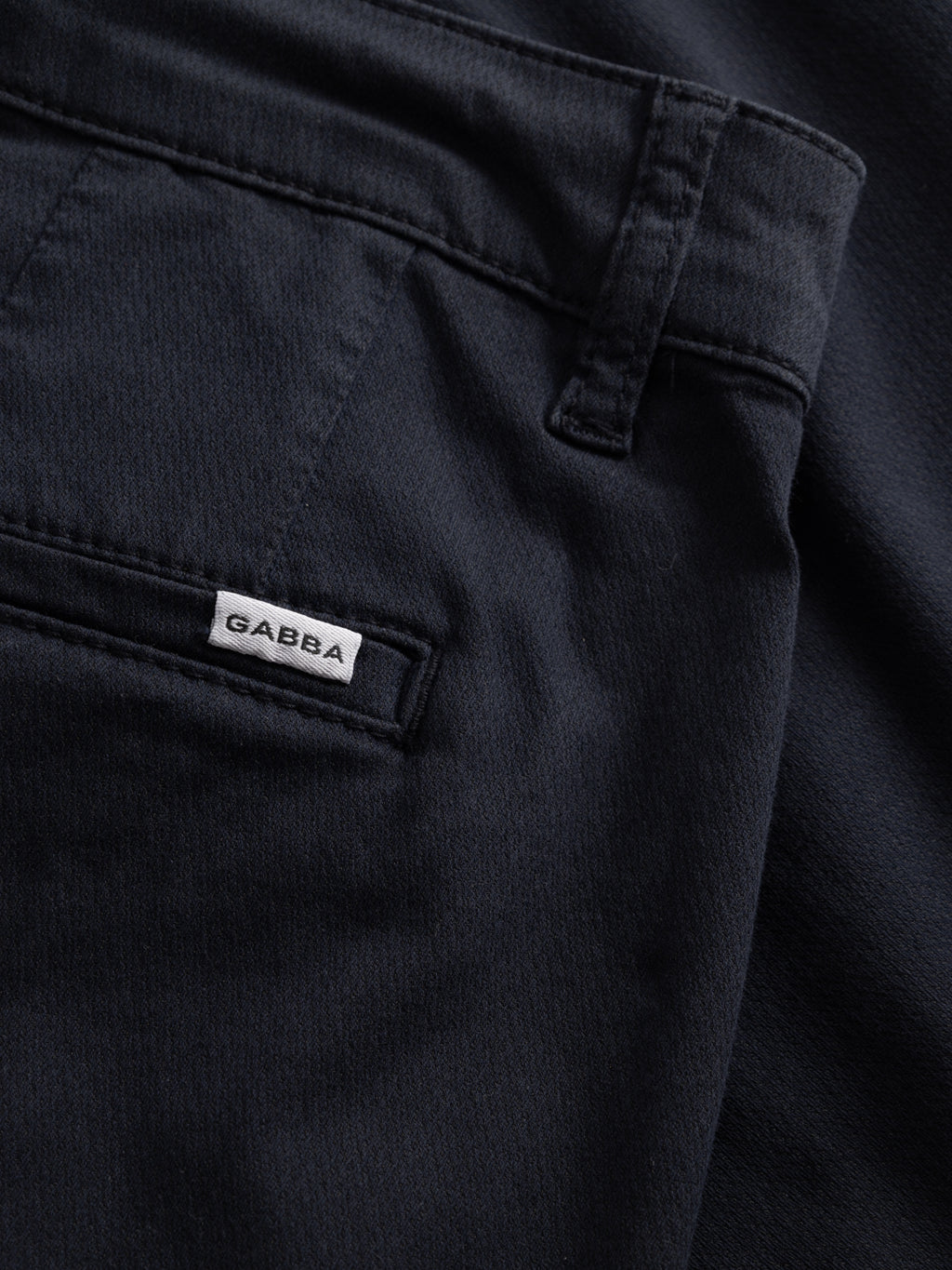 Close-up of Gabba GABjoli Nopleats Dale Shorts in Blue Black, showing a pocket with a small white GABBA label sewn onto the seam. The smooth fabric appears slightly textured.