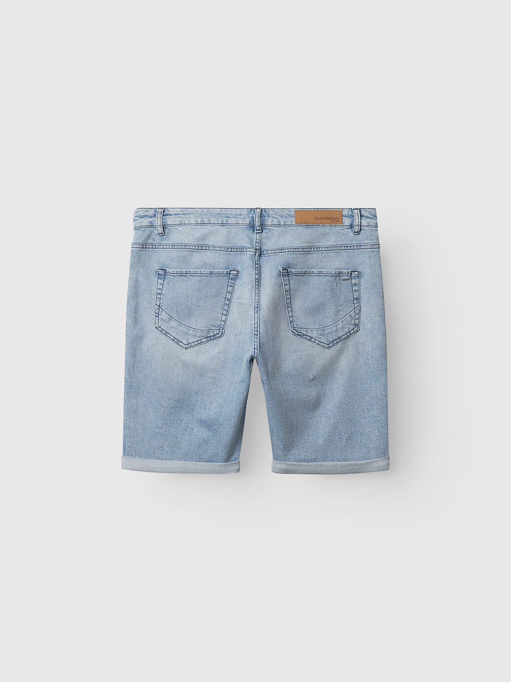 Back view of Gabba GABmarkus Derby Shorts in mid blue denim, featuring rolled hems, two back pockets, belt loops, and a tan leather patch on the waistband, shown against a plain white background.