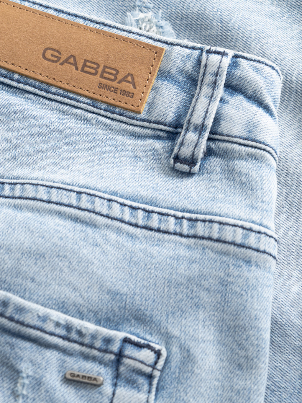 Close-up of GABmarkus Derby Shorts in mid blue denim by Gabba, showing a tan leather patch with the brand name and 