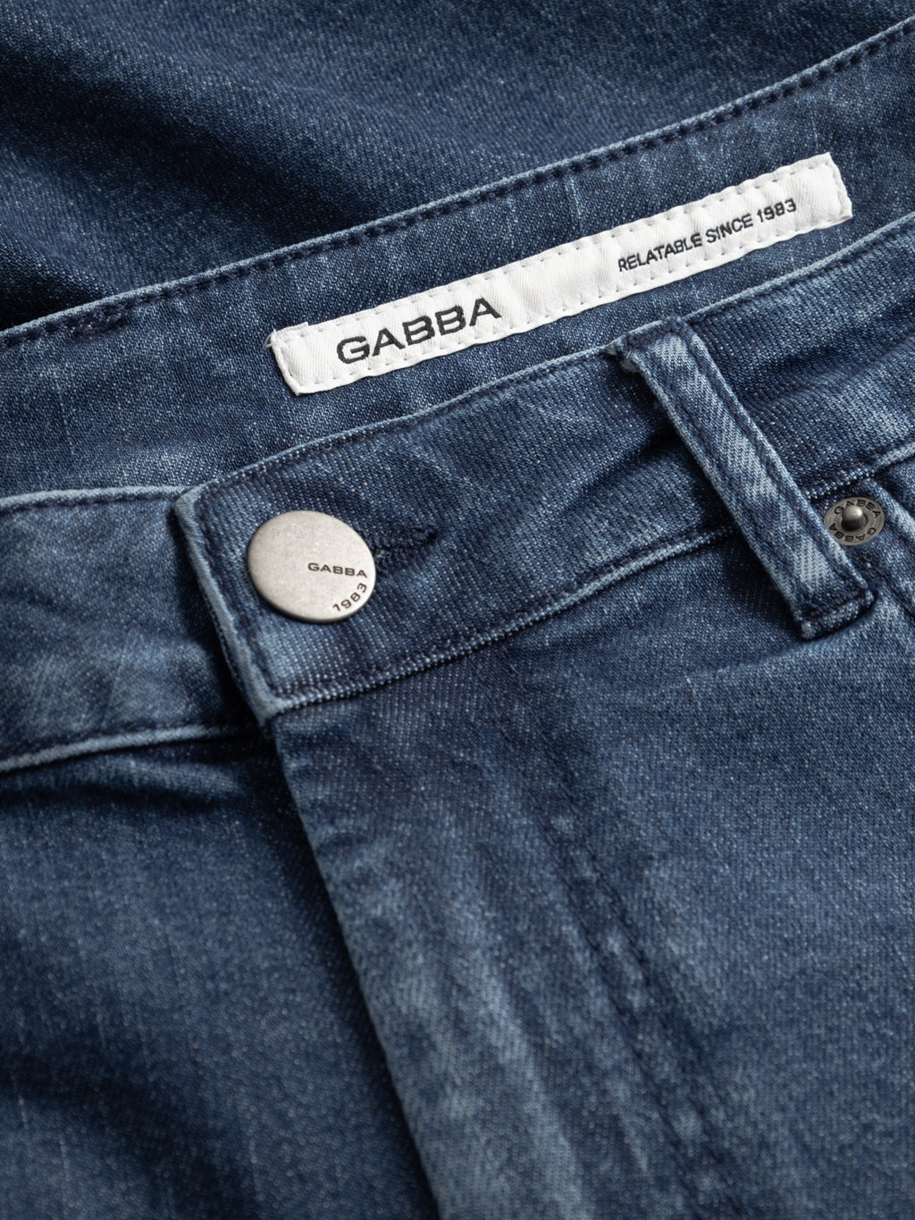 Close-up of GABmarkus Derby Shorts - Denim wash by Gabba, made from comfort-stretch denim with a metal button engraved with GABBA 1983 and a white inner label reading GABBA RELATABLE SINCE 1983.