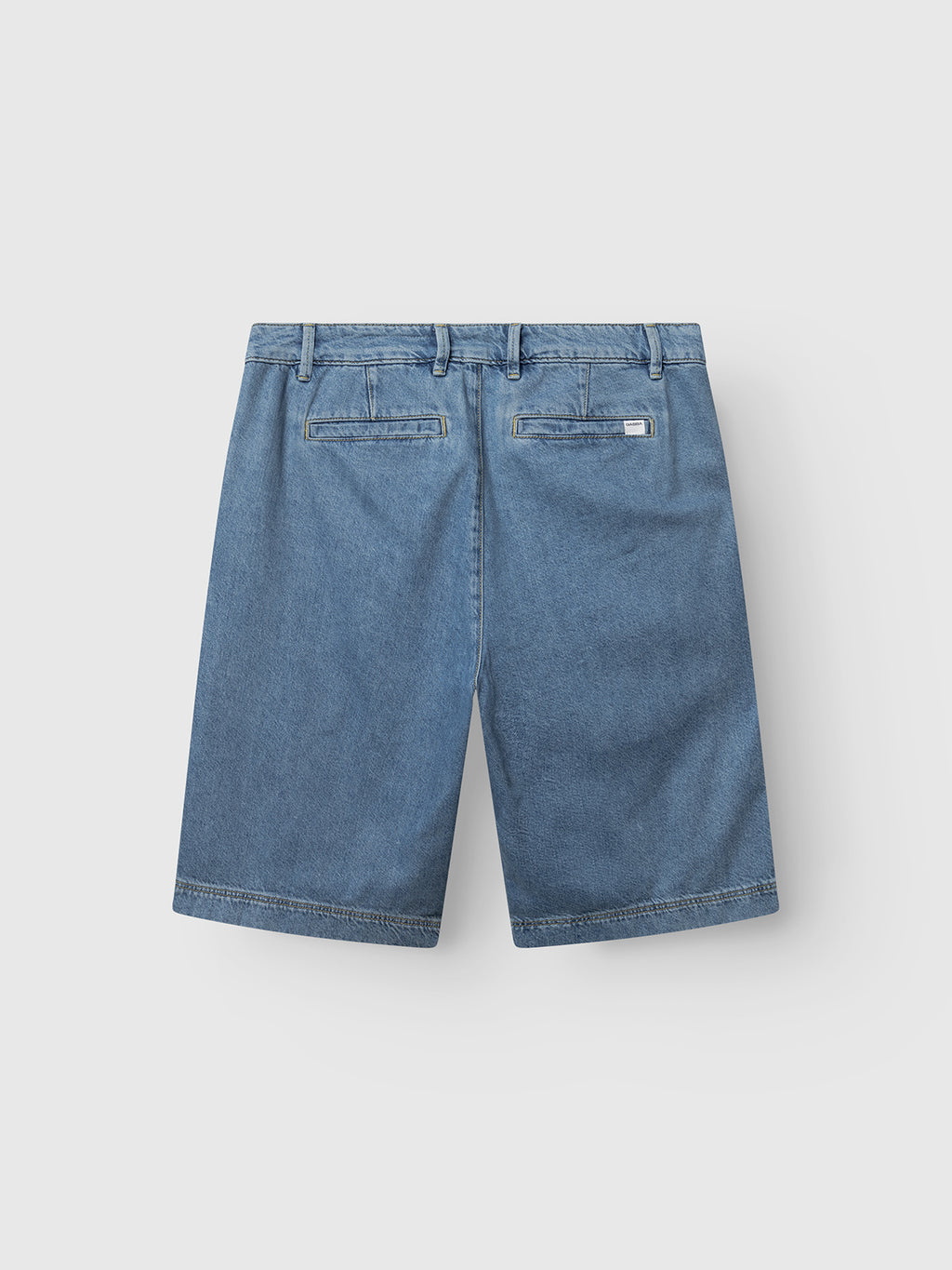 Back view of Gabba GABmoro PasBrook Shorts in denim wash, featuring a relaxed fit, belt loops, and two back pockets—one with a small white tag—displayed on a plain light gray background; an essential summer staple.