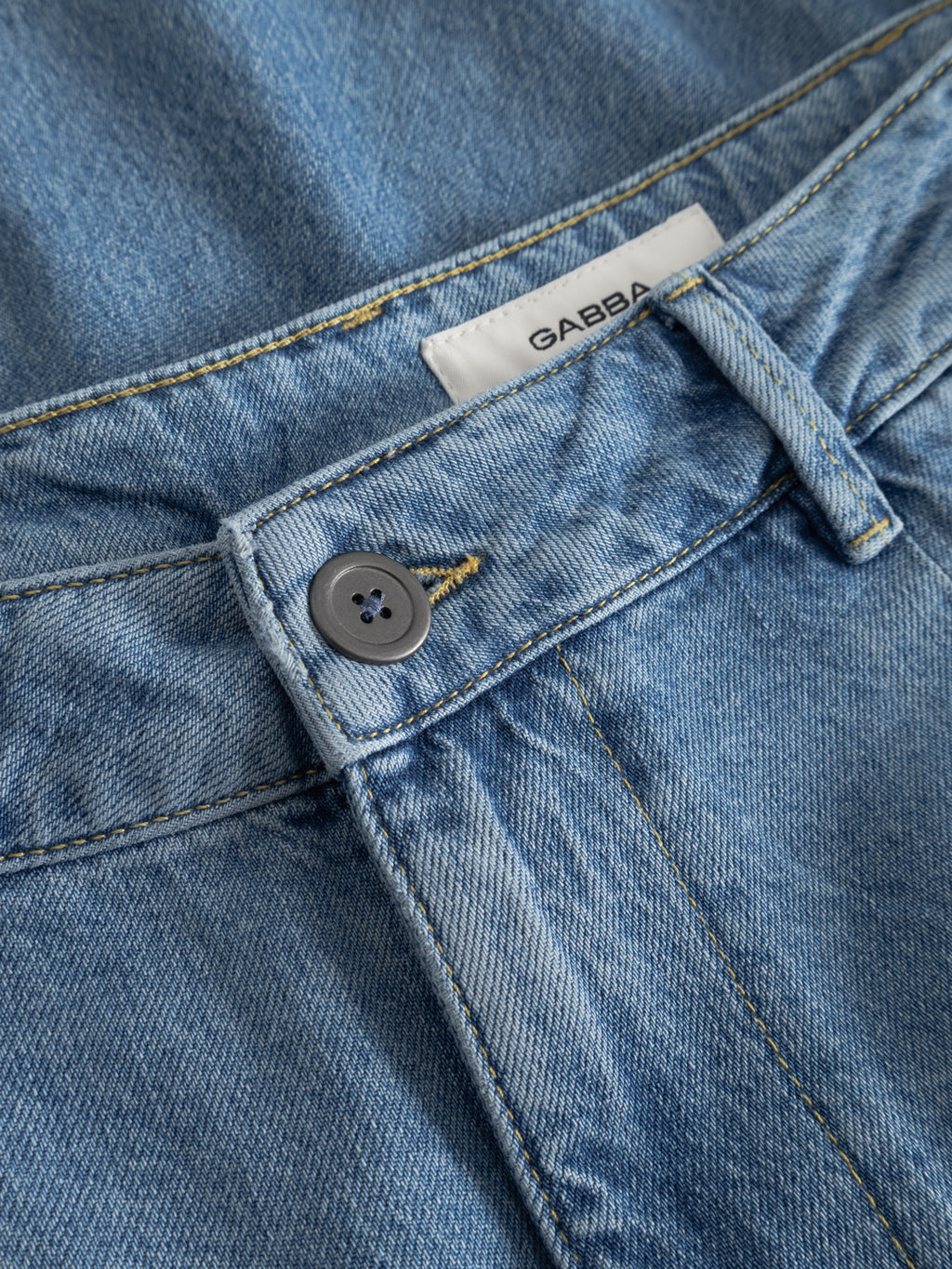 Close-up of Gabba GABmoro PasBrook Shorts in denim wash, featuring button, waistband, belt loop, and white label—a summer essential for relaxed fit and effortless style.