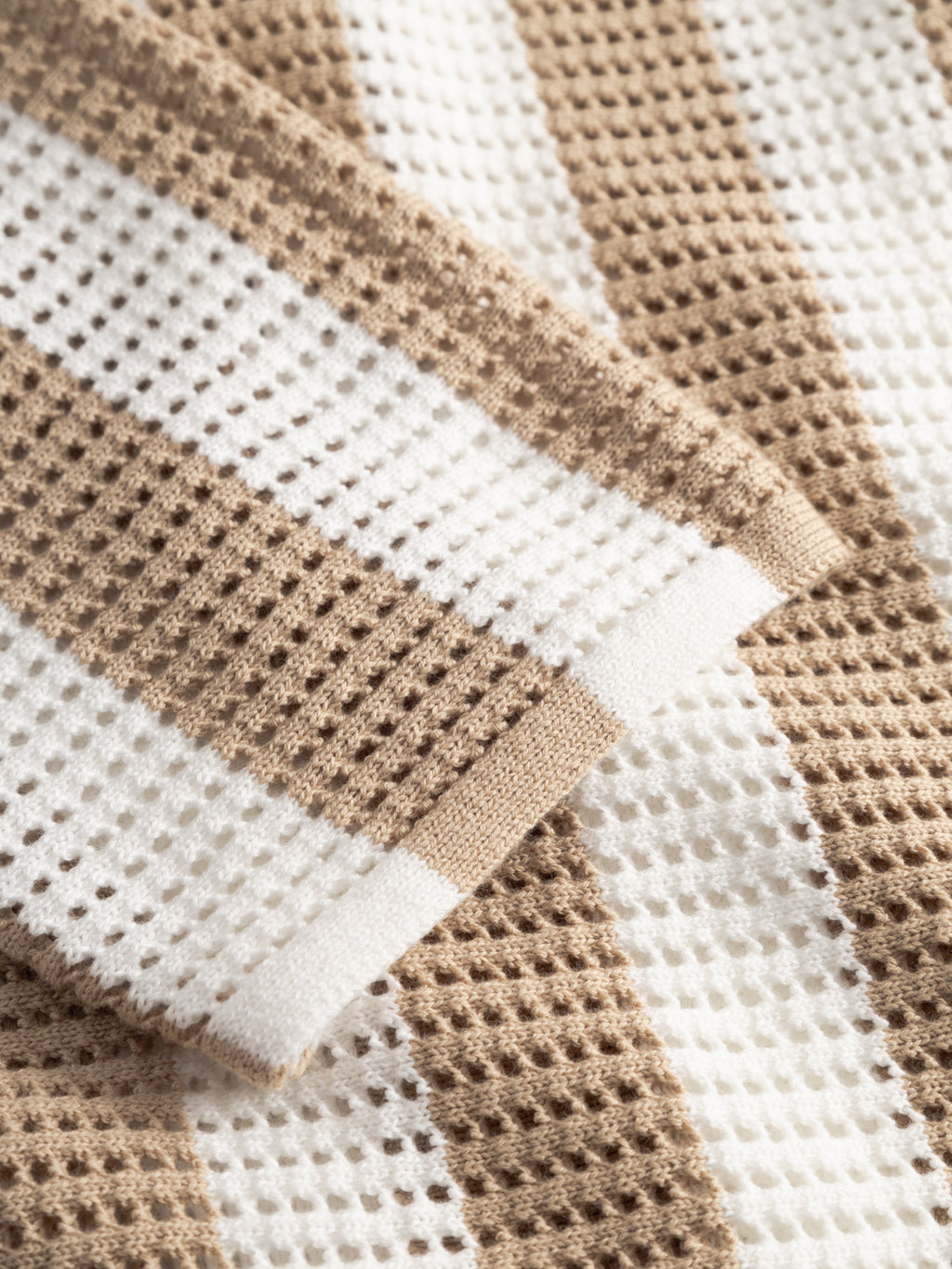 A close-up of the Gabba GABdezz Bold LS Knit in Beige Stripe shows its 100% cotton waffle weave fabric, featuring alternating beige and white stripes. The material looks soft and slightly folded.