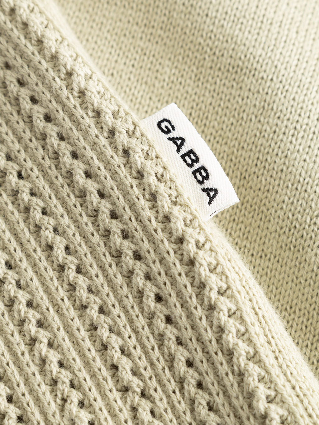 A close-up of the GABgeno Resort Bride SS Knit by Gabba in light green, featuring two distinct knit patterns and a small white tag with 