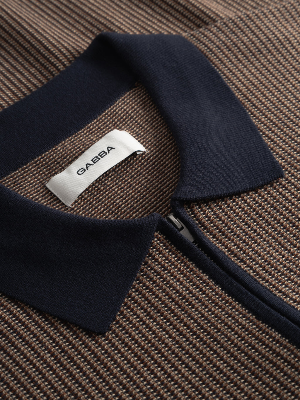 Close-up of the Gabba GABoswald Retro SS Knit - Navy, showcasing its textured brown and beige fabric with a navy blue collar and zipper. The label displays 