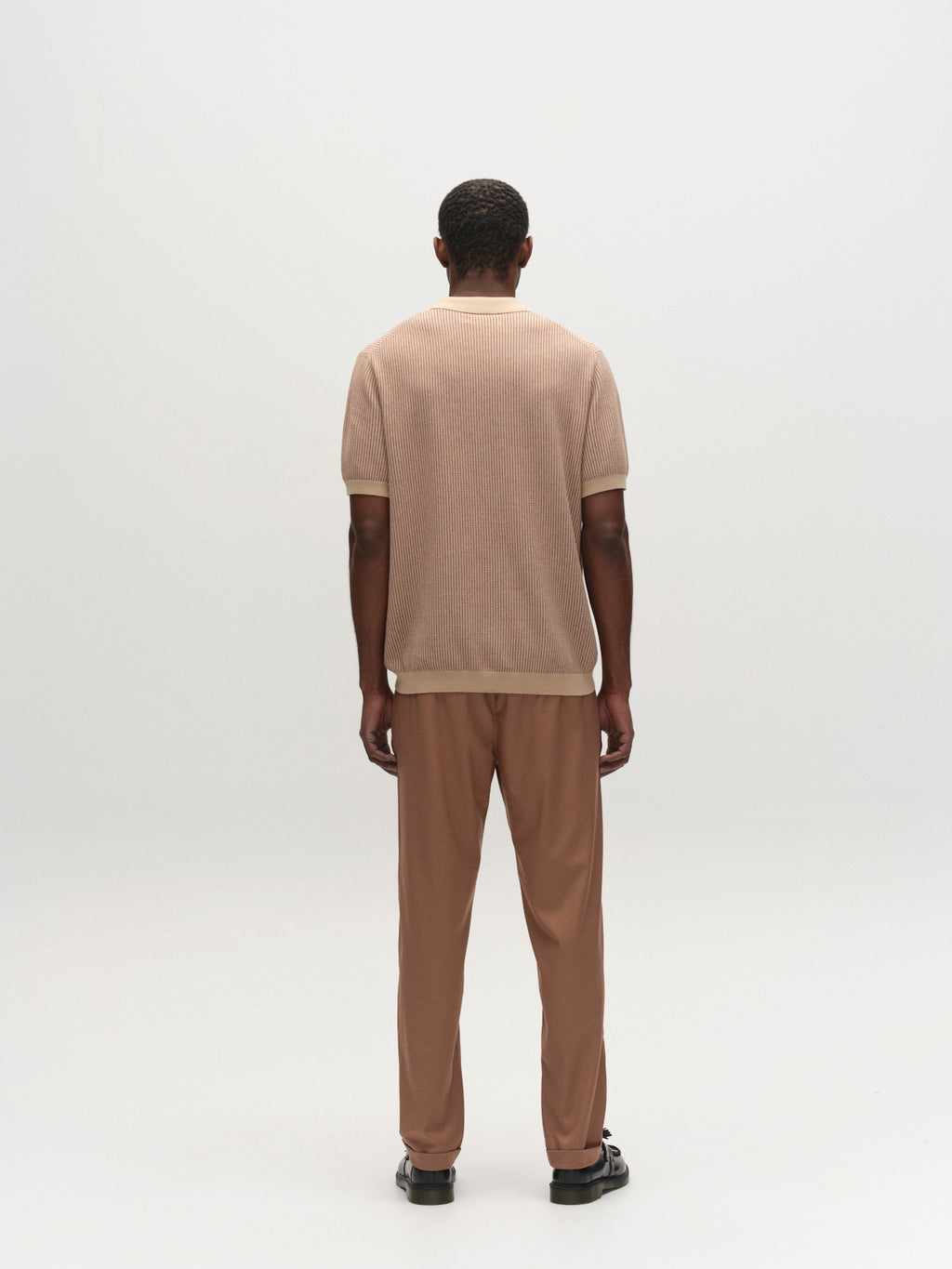 A man faces away from the camera wearing the Gabba GABoswald Retro SS Knit in Walnut, paired with matching pants and black shoes, set against a plain white background.