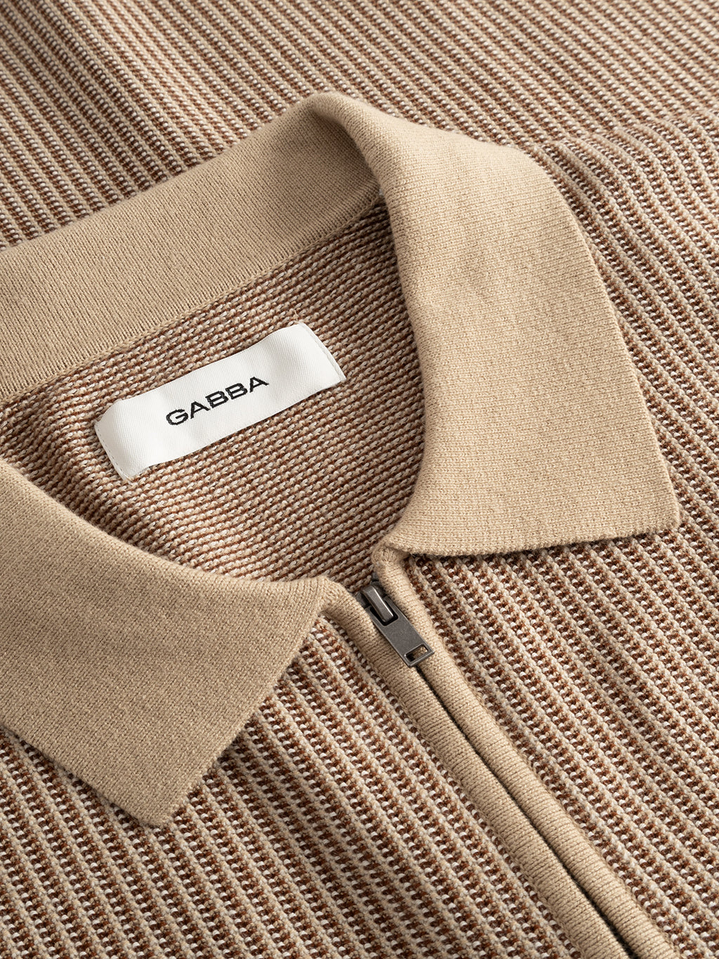 Close-up of the Gabba GABoswald Retro SS Knit polo in Walnut. This beige knit shirt features a zipper, collar, and a white Gabba label sewn inside the neckline; its textured knit is clearly visible.