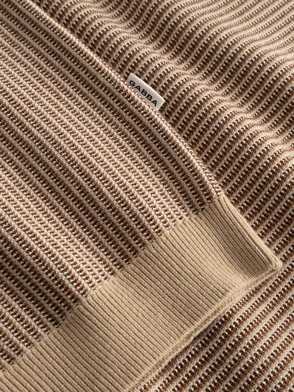 A close-up of the Gabba GABoswald Retro SS Knit in Walnut shows beige and brown ribbed fabric with a striped texture, a solid beige cuff, and a small white Gabba tag.