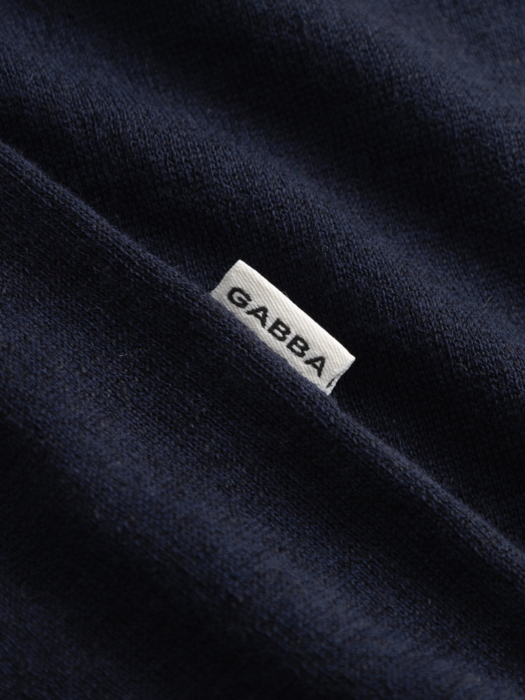 A close-up of the GABvento Dush SS Knits - Navy by Gabba, featuring lightweight navy blue flat knit fabric and a small white tag with 