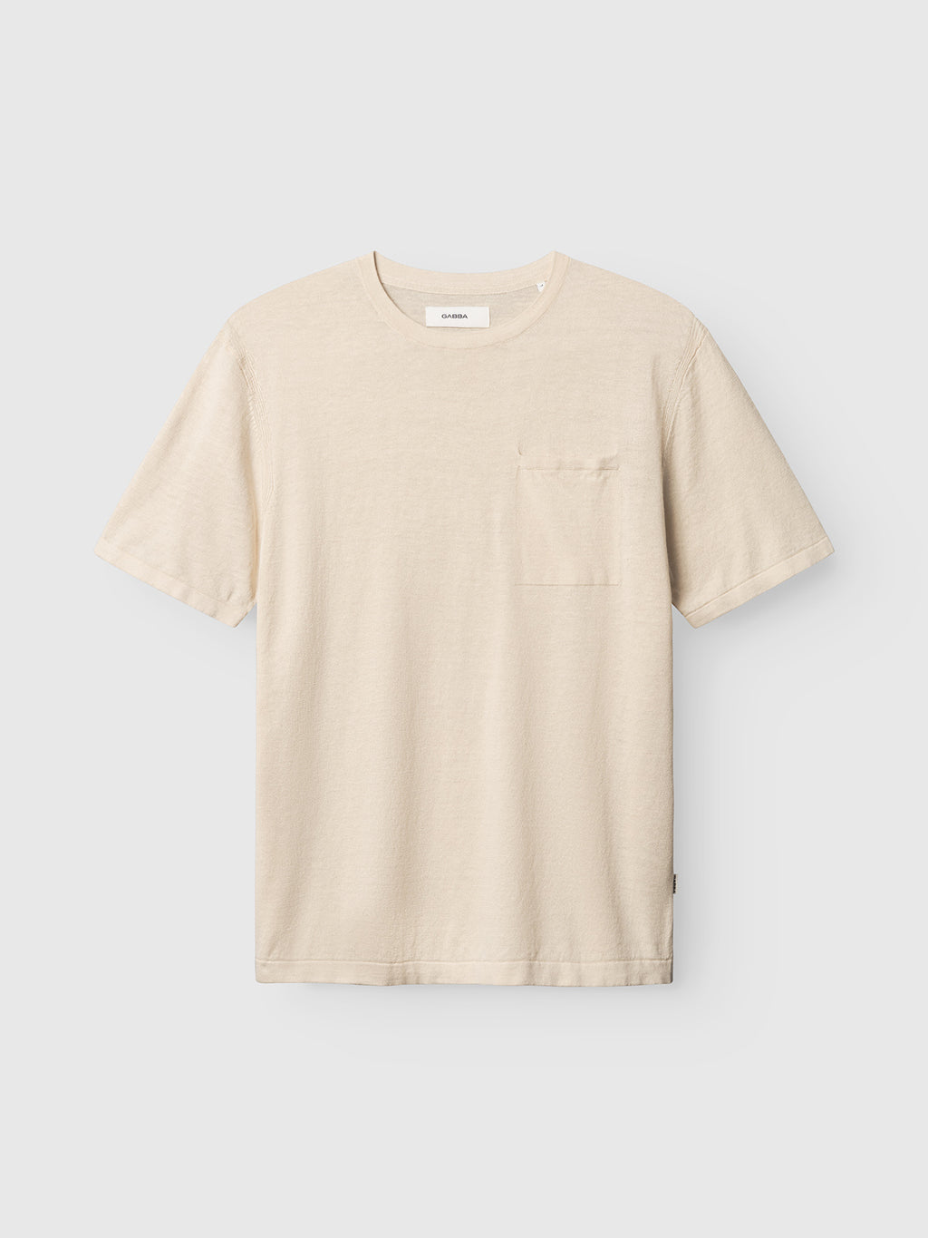 The Gabba GABvento Dush SS Knits in Sand Mel. is a lightweight, cream short-sleeve knit t-shirt with a small chest pocket, shown on a light gray background.
