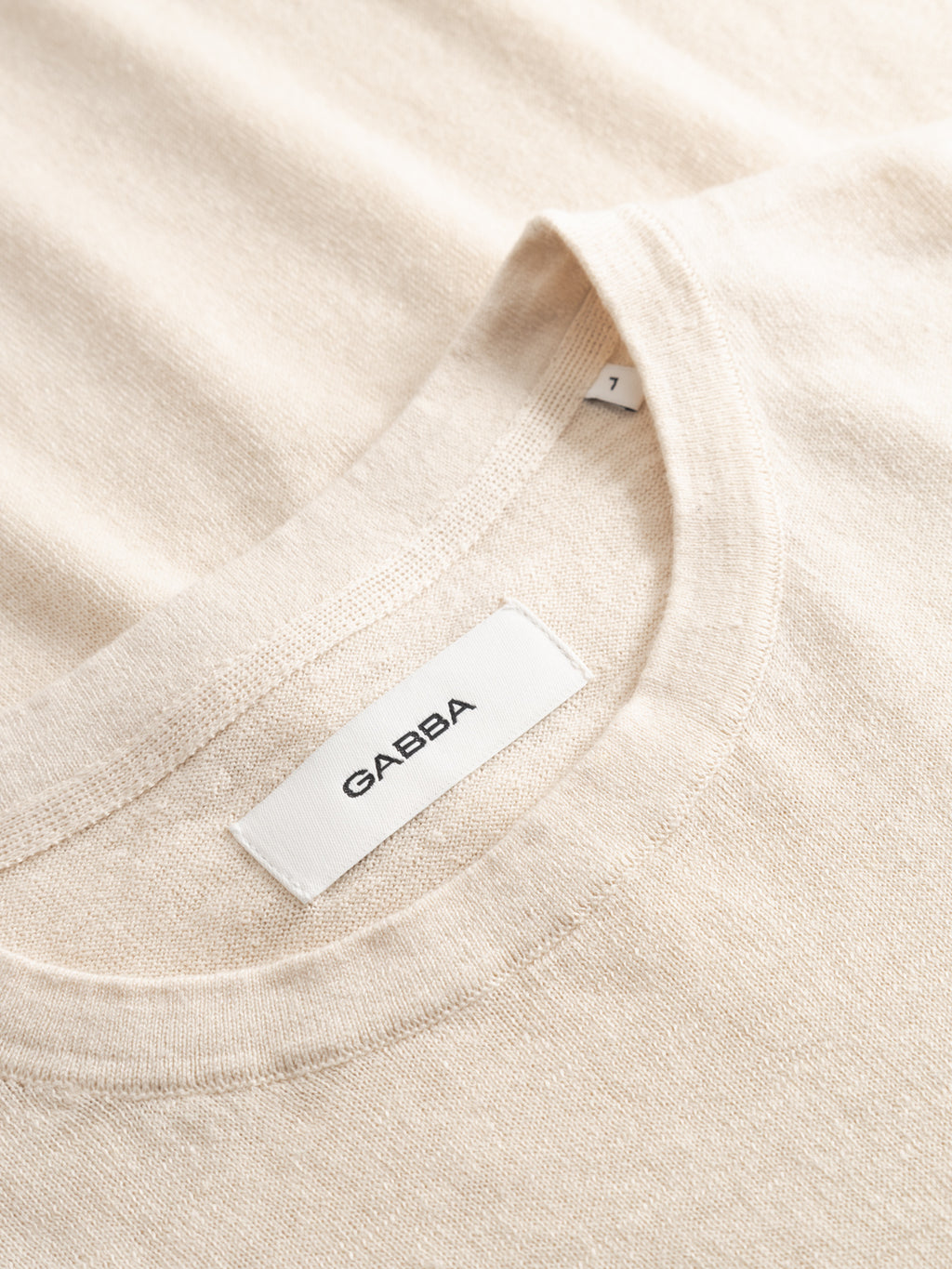 Close-up of the Gabba GABvento Dush SS Knits in Sand Mel., a light beige short-sleeve knit T-shirt with a white collar label showing 