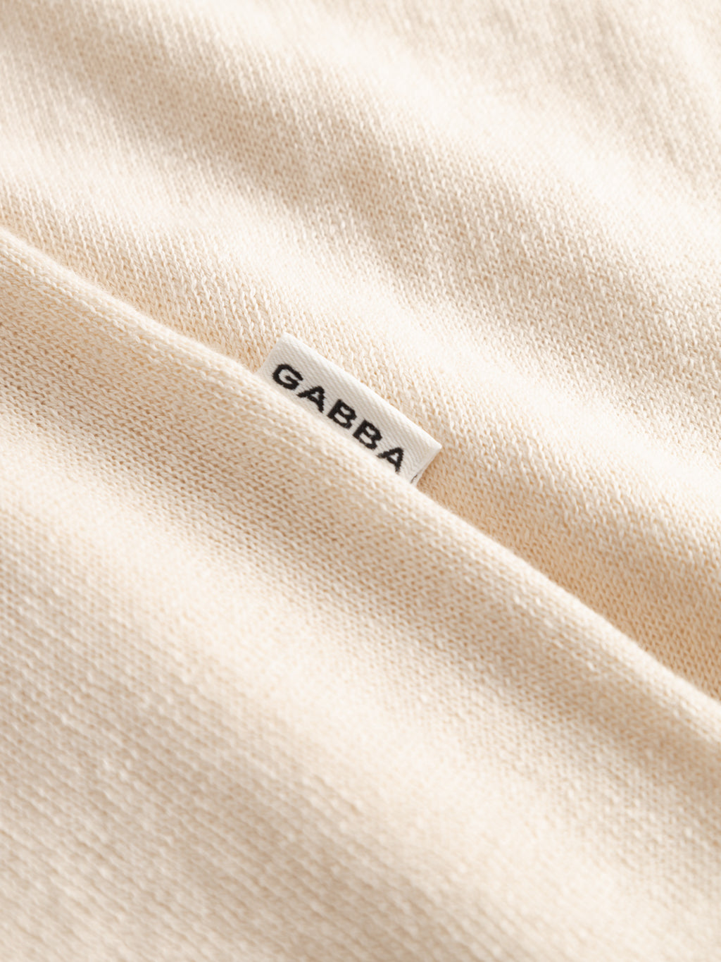 Close-up of the GABvento Dush SS Knits in Sand Mel by Gabba, showcasing its soft, lightweight beige flat knit fabric with a small white 