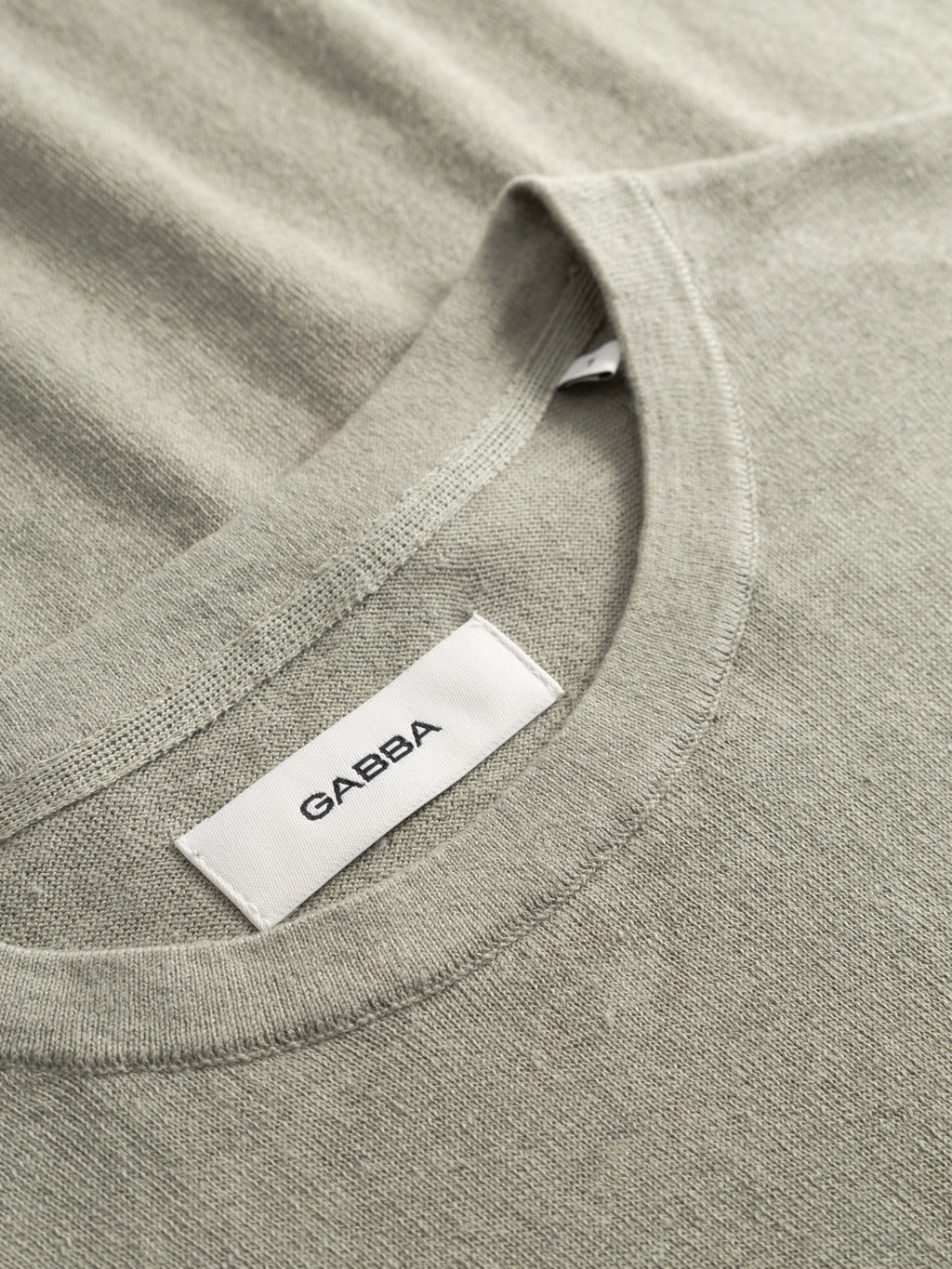 A close-up of the light green, lightweight GABvento Dush SS Knits T-shirt by Gabba, featuring a flat knit texture and a white Gabba label sewn into the collar. The fabric appears soft and textured.