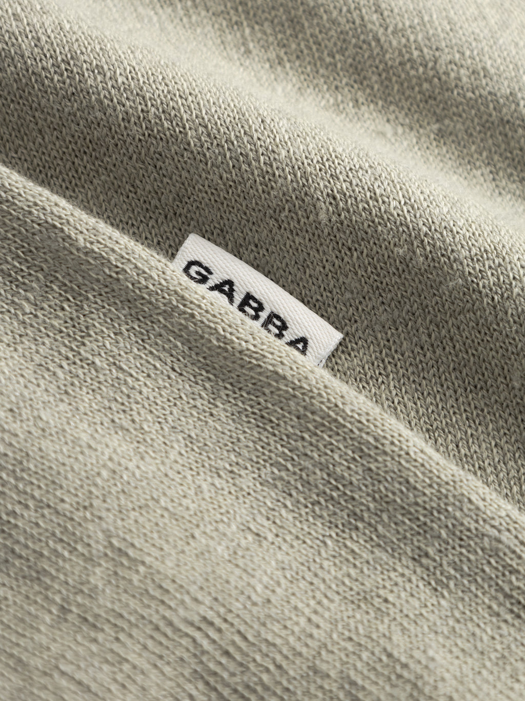 Close-up of a textured, light green lightweight flat knit fabric from the Gabba GABvento Dush SS Knits, featuring a small white label with 