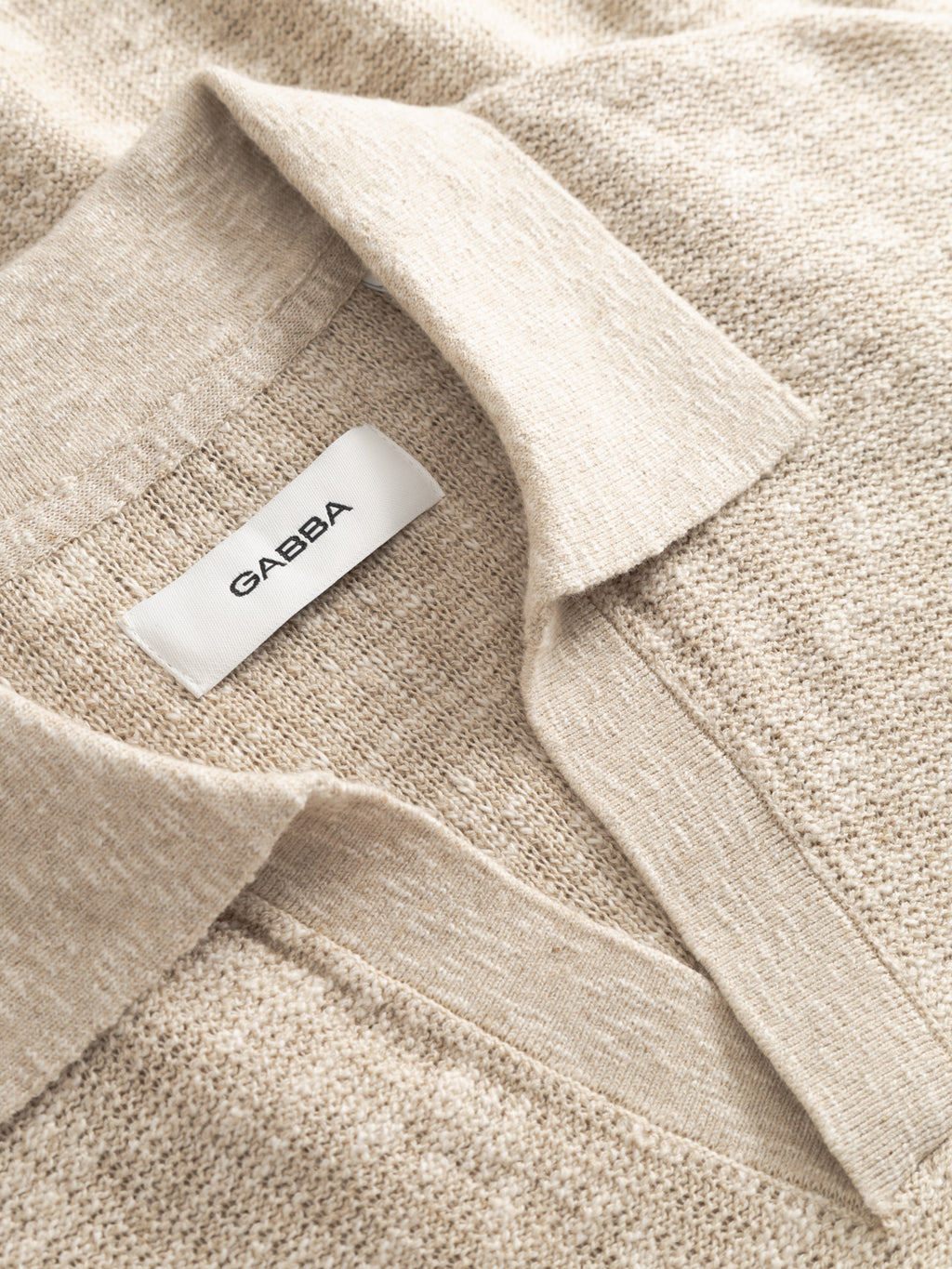 Close-up of the Gabba GABcross Alto SS Knit in ecru, featuring a textured beige knit with a collar. A white inner label displays the brand name 