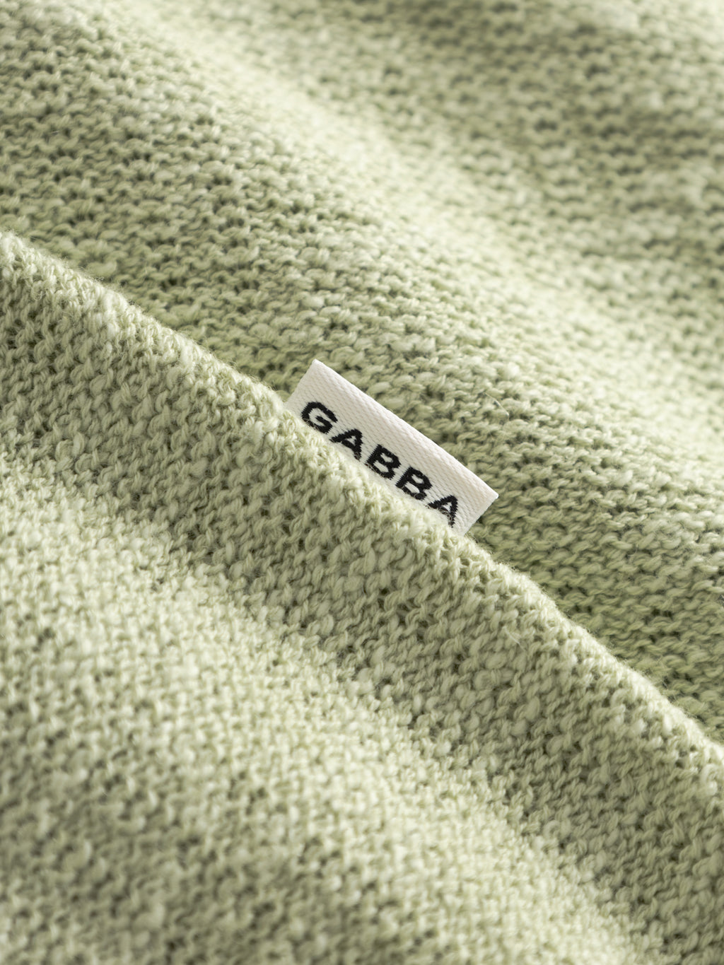 A close-up of the textured Alfa Green GABcross Alto SS Knit by Gabba, showing a small white Gabba tag partially tucked into a seam.