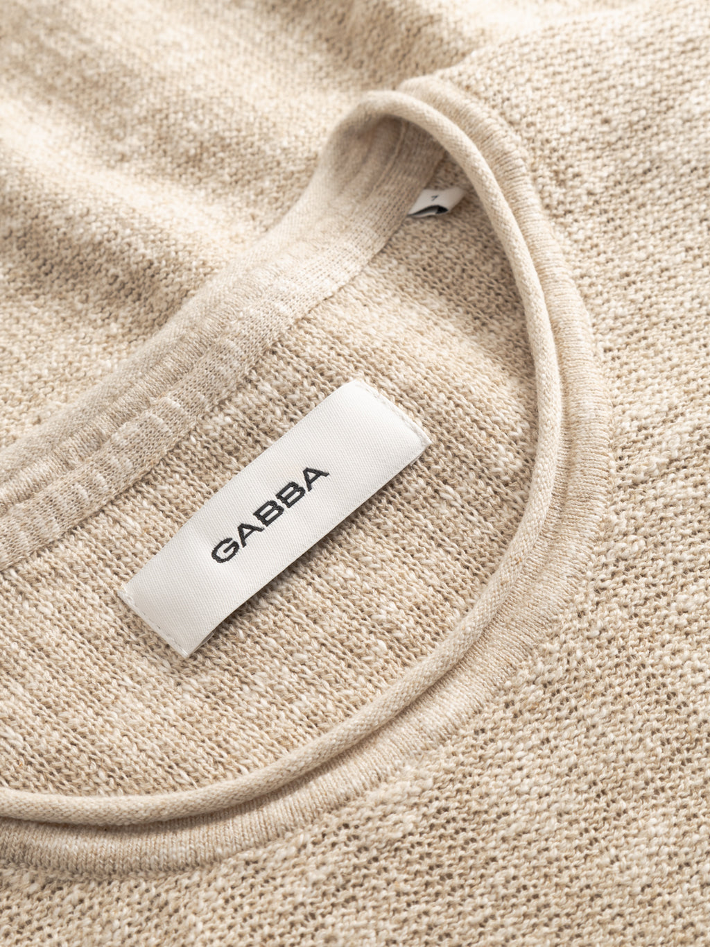 Close-up of the inside neck area of an ecru GABnigel Alto SS Knit sweater by Gabba, featuring a white label with 