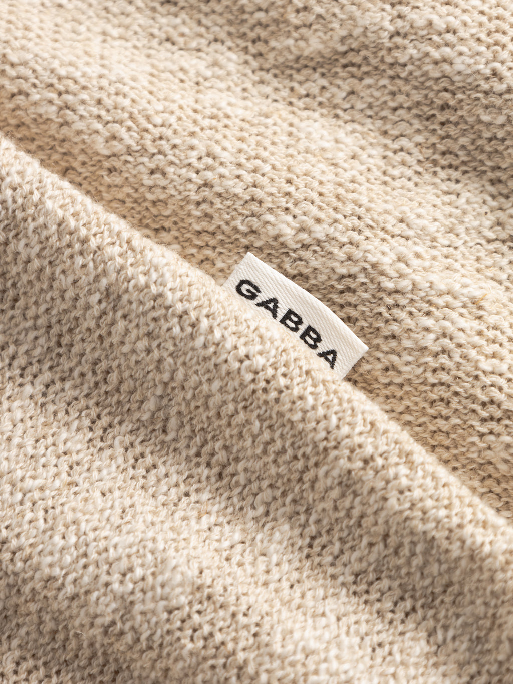 A close-up of the textured ecru GABnigel Alto SS Knit fabric from Gabba, featuring a small white label with 