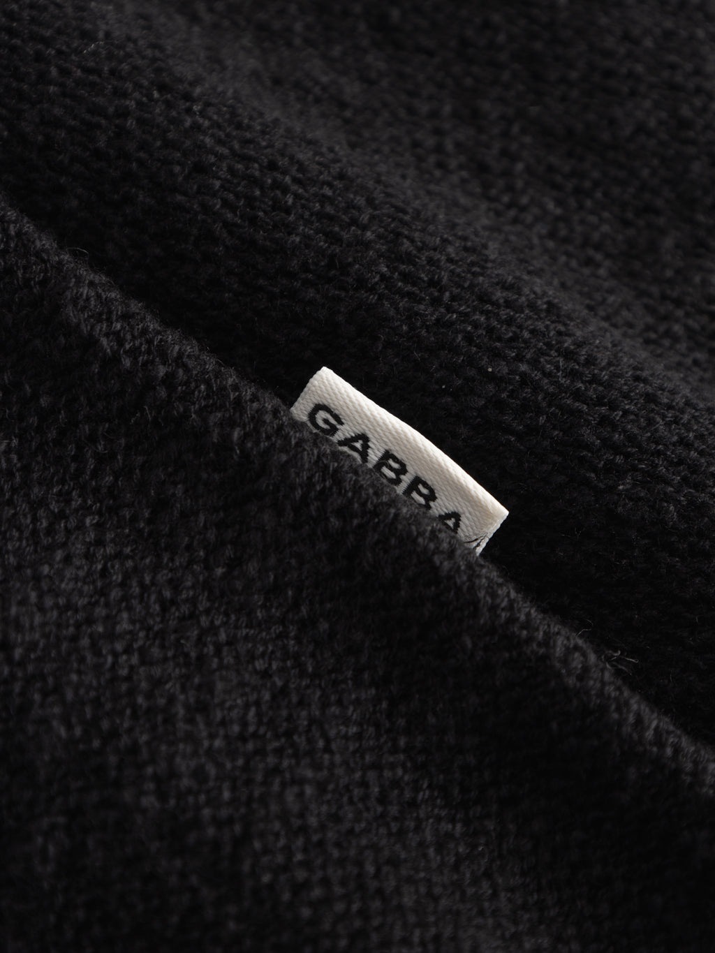 Close-up of a black textured fabric from the Gabba GABnigel Alto SS Knit, with a small white label partially visible showing the brand name.