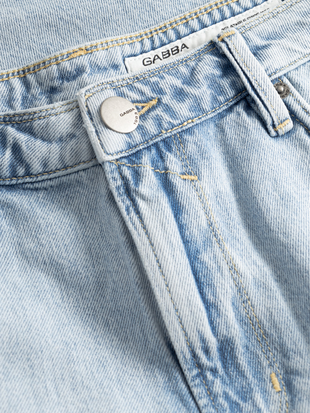 Close-up of Gabba GABmox Tona Shorts in light blue denim, highlighting the relaxed fit, twill fabric, waistband with engraved metal button, zipper fly, belt loop, and white 