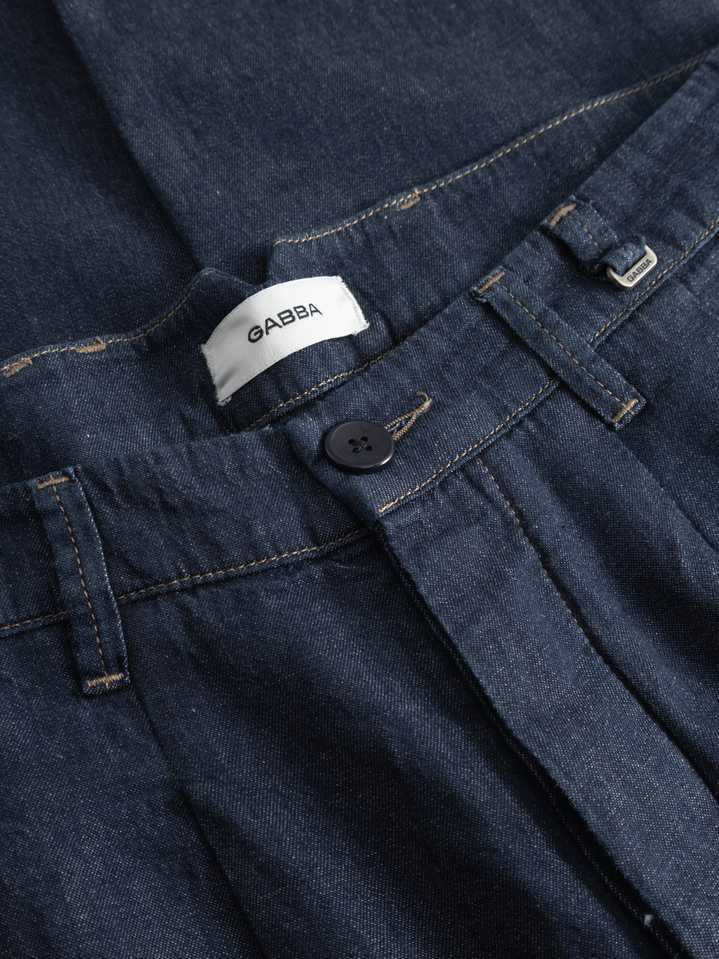 Close-up of Gabba’s GABfirenze Geky Denim Cropped Pant in denim blue, with classic tailoring, black button, visible waistband and belt loops, white 