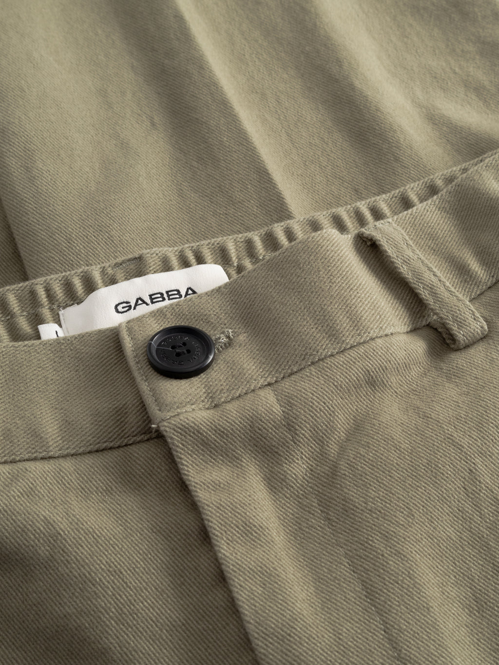 Close-up of GABdenver Elastic Twill Pant by Gabba in green, featuring a black button at the waistband and a white Gabba label inside. Made from soft, slightly textured stretch twill for comfort.