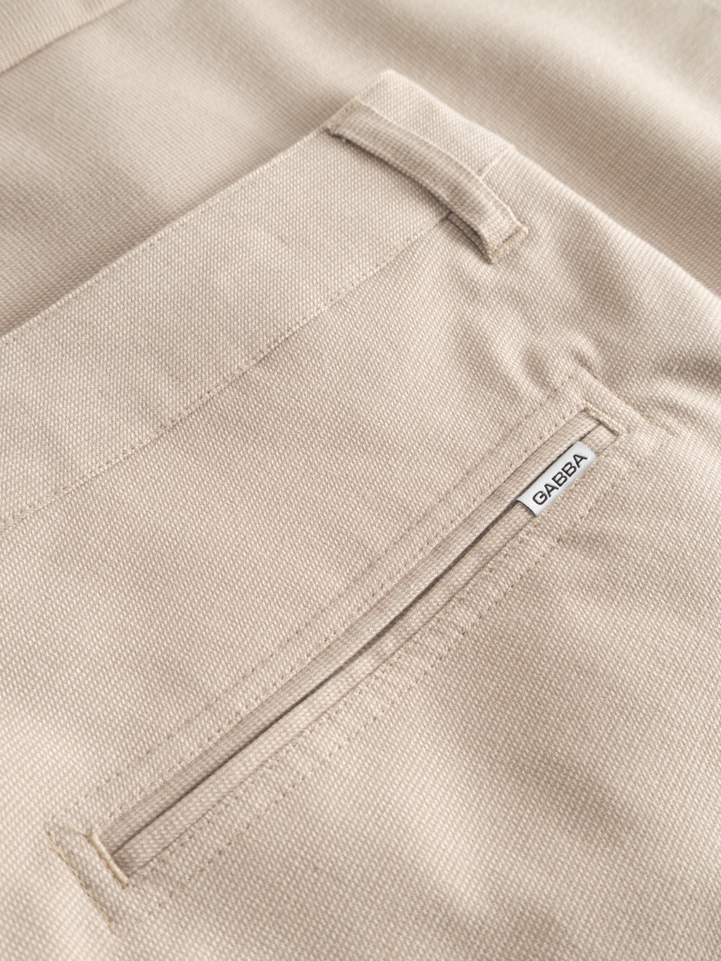 Close-up of the back pocket on GABjet Deme Shorts - Birch by Gabba, featuring a subtle textured beige fabric, a refined button closure, and a small white Gabba label sewn near the top for a classic touch.