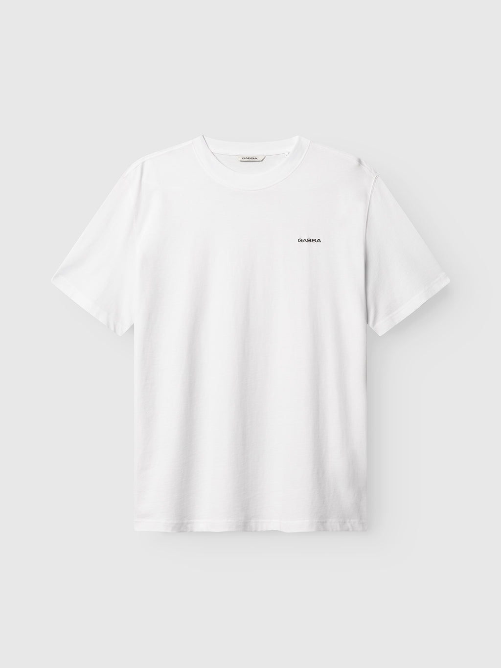 The Gabba GABnigel Boxy Logo GOTS SS in white is a short-sleeve T-shirt featuring a small logo on the left chest, shown against a light gray background.