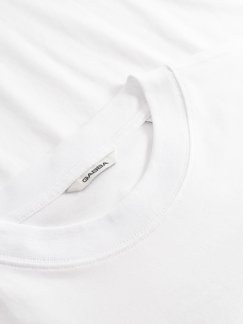 Close-up of the collar and neckline of the Gabba GABnigel Boxy Logo GOTS SS t-shirt in white, featuring a white tag with the Gabba brand name sewn inside. The fabric looks soft and smooth.