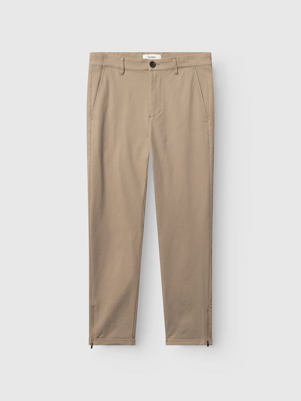 The Gabba GABpaul L.C. Zip Crop Doby Pant in Sand features a straight-leg fit, front pockets, button and zip closure, and small zippered ankle slits, shown laid flat on a white background.