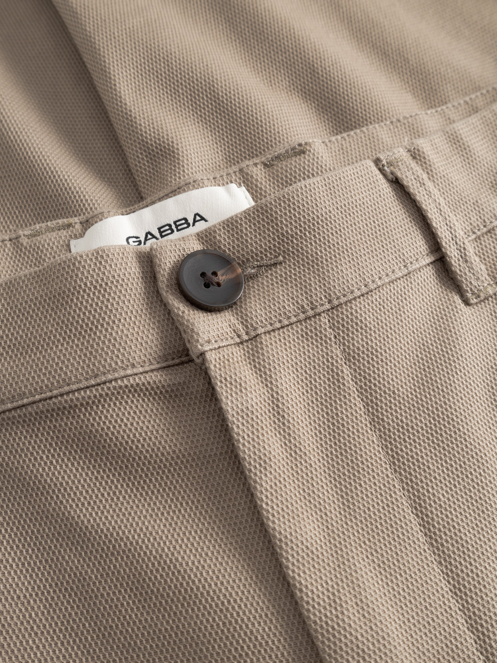 Close-up of the GABpaul L.C. Zip Crop Doby Pant in sand by Gabba, featuring beige textured fabric, a black button, and a partially visible white 
