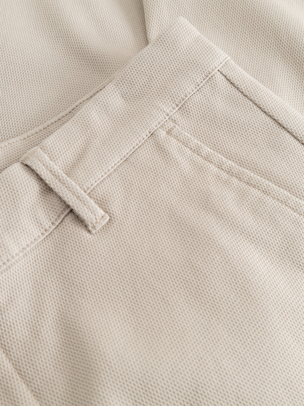 Close-up of the Gabba GABpaul L.C. Zip Crop Doby Pant in Lt. Sand, highlighting the textured waistband, belt loop, and front pocket, with overlapping fabric in the background.