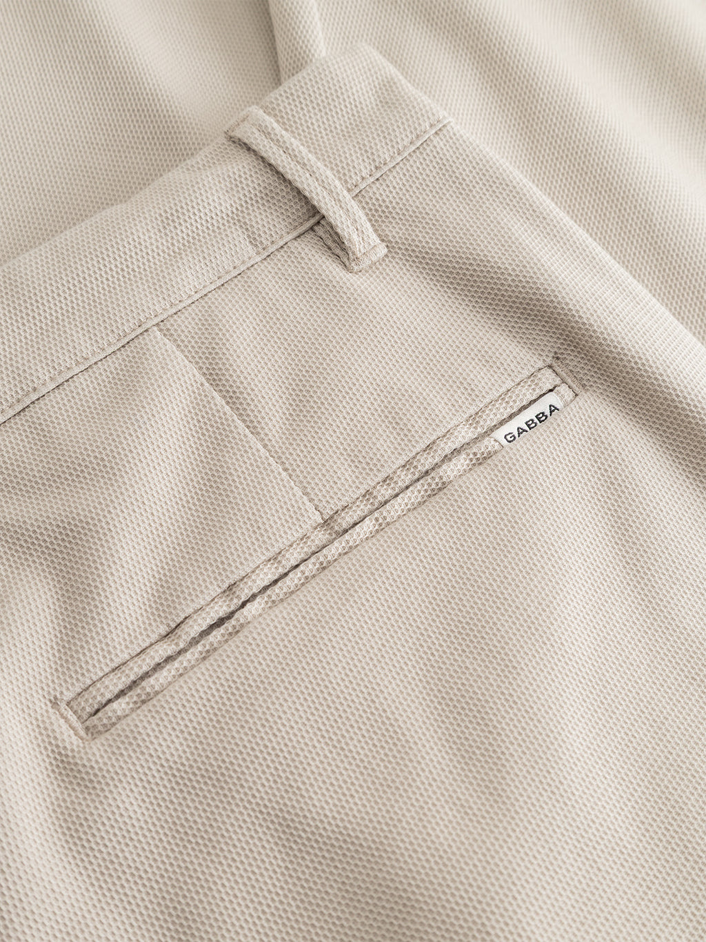 Close-up of the textured fabric pocket on Gabba’s GABpaul L.C. Zip Crop Doby Pant in Lt. Sand, showing a small white Gabba tag near the opening.