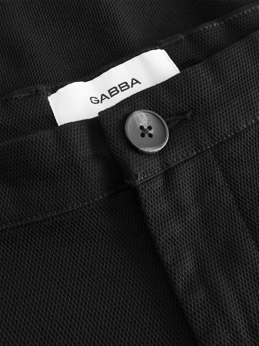 Close-up of the Gabba GABpaul L.C. Zip Crop Doby Pant in blue black, featuring a textured fabric, black button, and an inner waistband label reading GABBA.