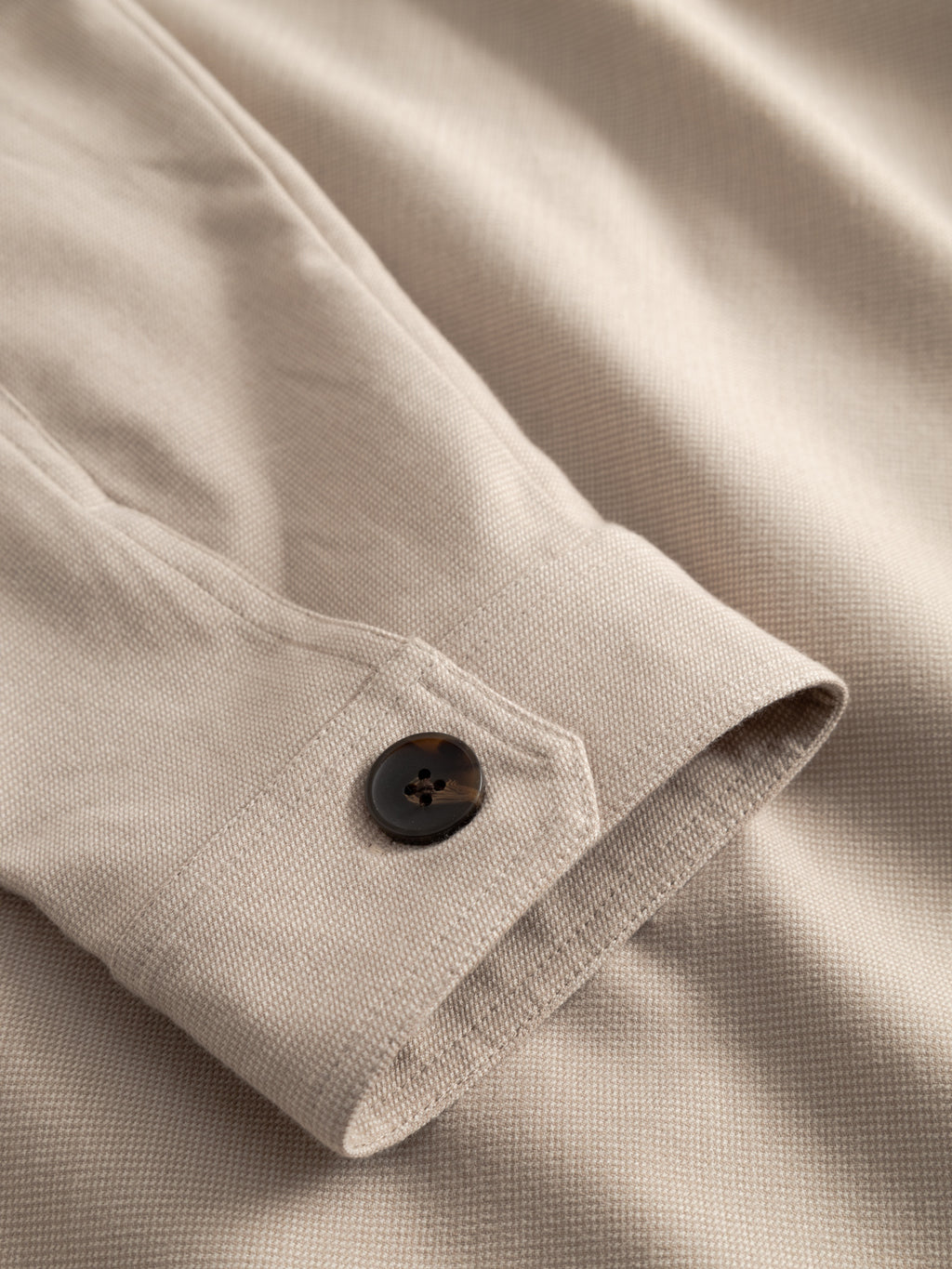 Close-up of the Gabba GABtogger Base Deme LS Overshirt in Birch, featuring a beige micro-pattern woven fabric sleeve with visible stitching and a single dark cuff button—offering a tailored look, perfect for layering.
