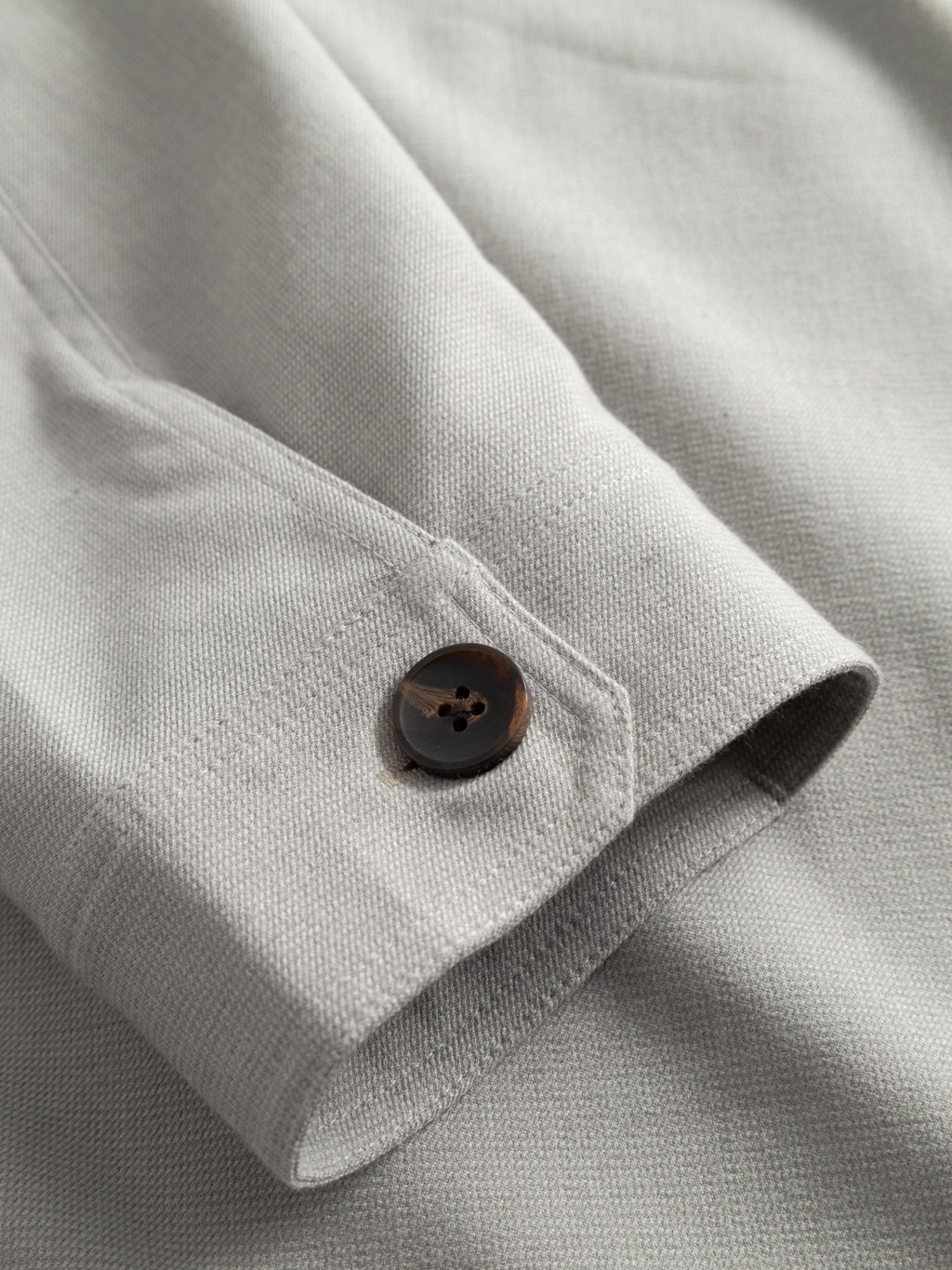 A close-up of the Gabba GABtogger Base Deme LS Overshirt in Mineral Gray shows its micro-pattern woven fabric, dark brown cuff button, and visible stitching—ideal for stylish seasonal layering.