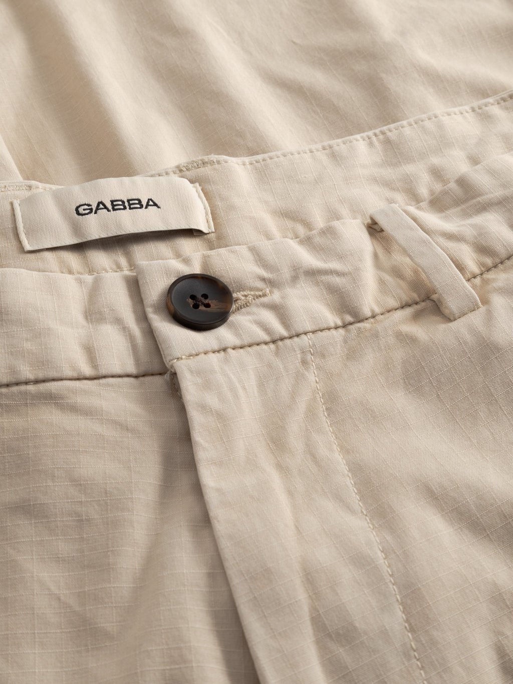 Close-up of GABjoli Cargo Ribstop Shorts in Birch by Gabba, showcasing a button closure, belt loops, visible seams, and an inner white fabric label—ideal for versatile everyday wear.
