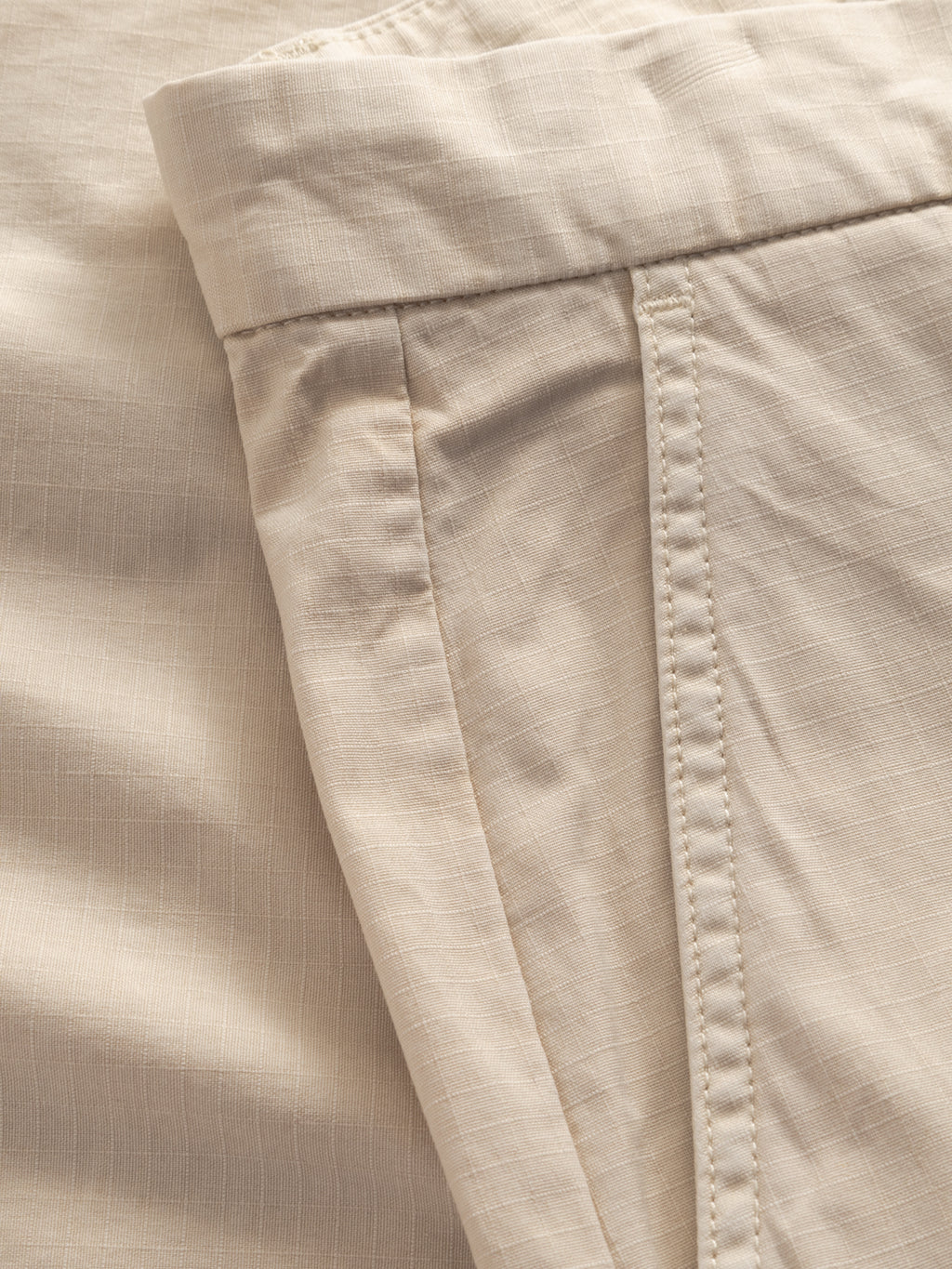 Close-up of Gabba’s GABjoli Cargo Ripstop Shorts in Birch, featuring lightweight textured fabric with visible stitching and a subtle grid pattern. Details of waistband, pocket, and seams highlight their versatile everyday style.