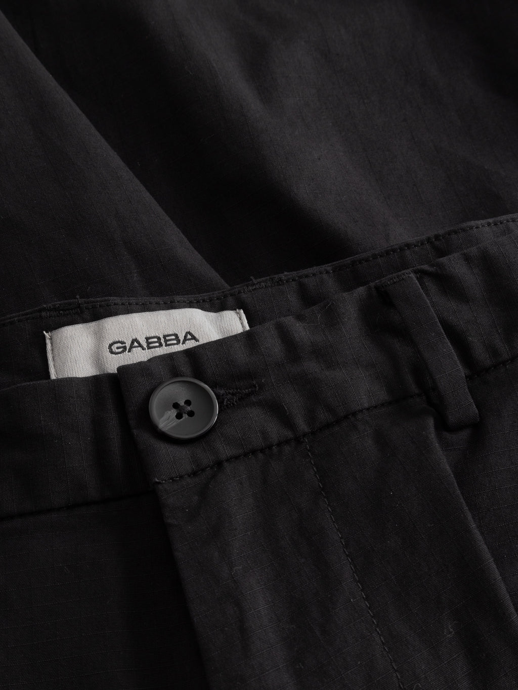 Close-up of GABjoli Cargo Ripstop Shorts in black by Gabba, featuring a waistband with black button, visible white Gabba label, and versatile everyday style—perfect for pairing with relaxed tops or side cargo pockets.