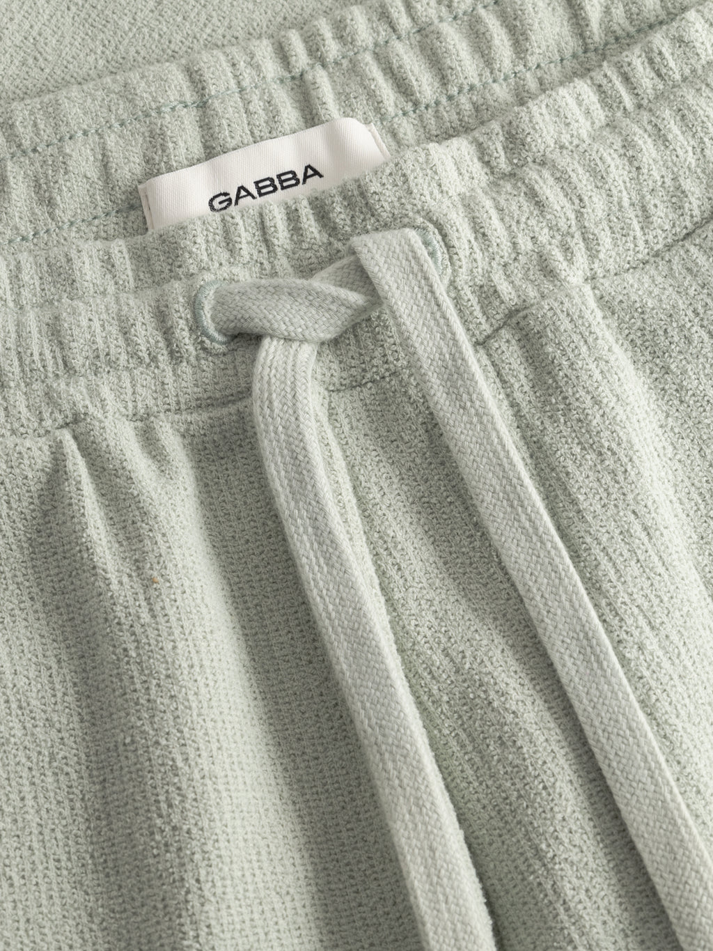 Close-up of GABtommi Towel Shorts in Mineral Gray by Gabba, featuring textured terry cotton, an elastic waistband with matching drawstring, and a white label showing the Gabba brand.